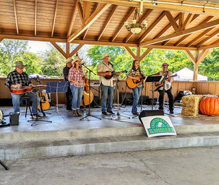 Band playing instruments on a wooden stage with a 'Piney Woods Ranch' sign.
